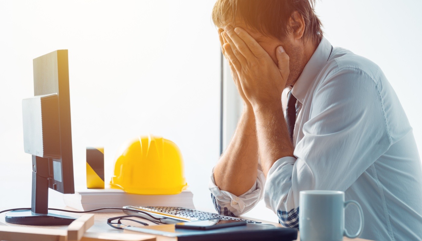 Trades contractor with head in hands at desk, reacting to crisis; construction software flexibility