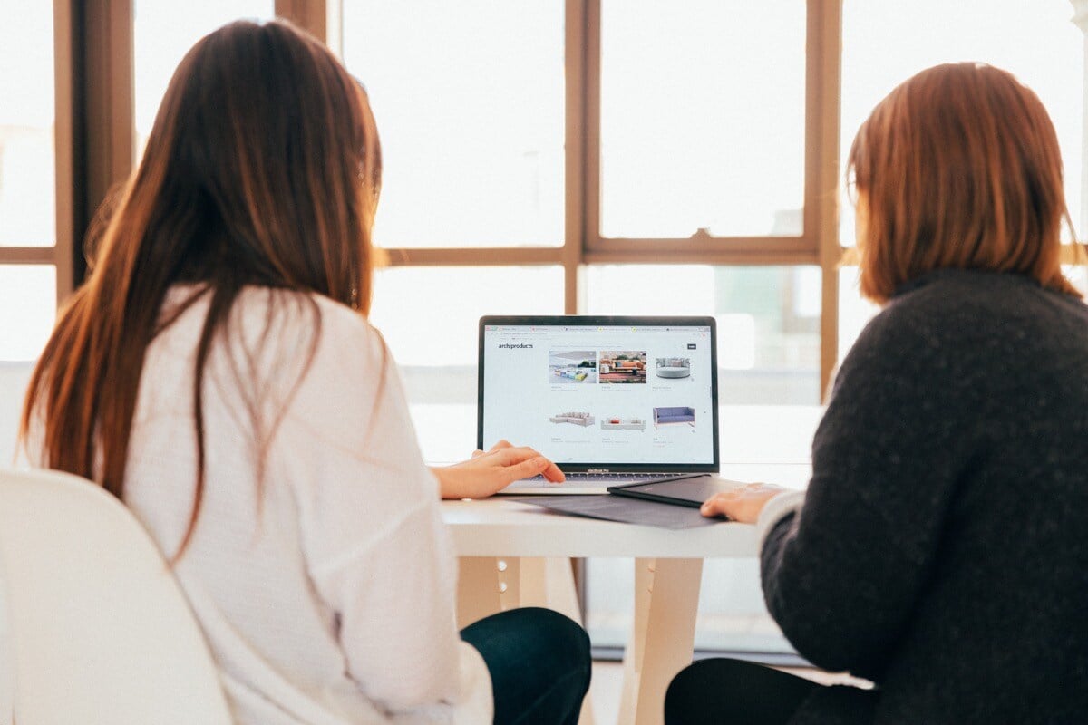 Two seated women facing laptop; unorganized data costs concept
