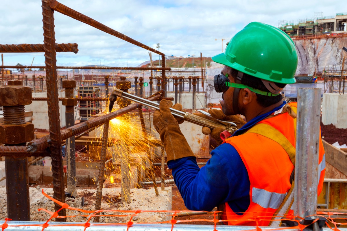 Construction worker welding hardware at site; construction businesses software concept