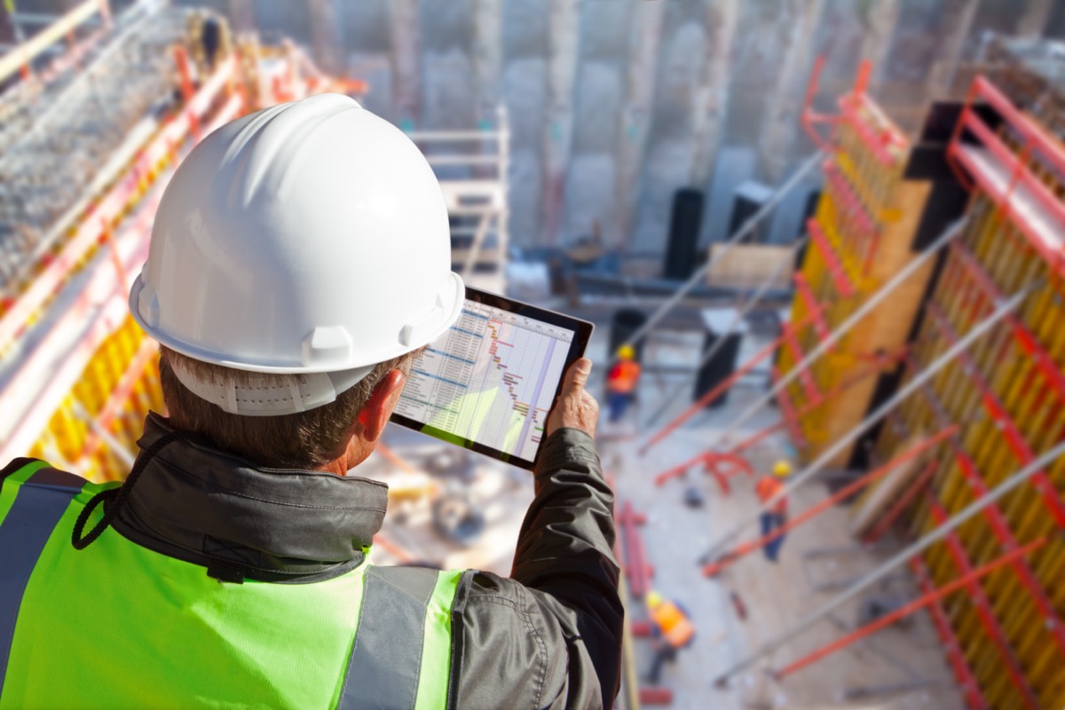 Architect with hardhat on construction site checking tablet; simple construction software concept