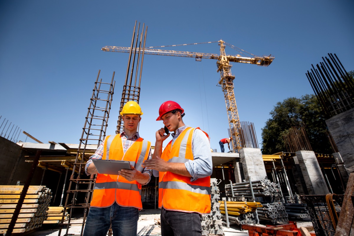 Structural engineer and architect in orange work vests and hard hats on construction site; software automation concept