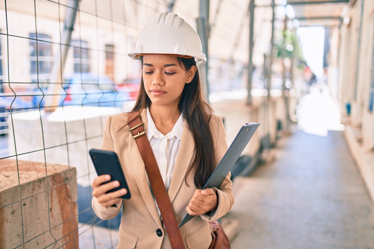 Architect on site with hard hat using smartphone; subcontracting business concept