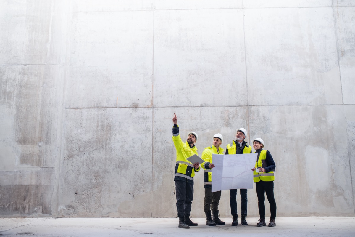 A group of engineers standing near concrete wall on construction site; construction company longevity concept