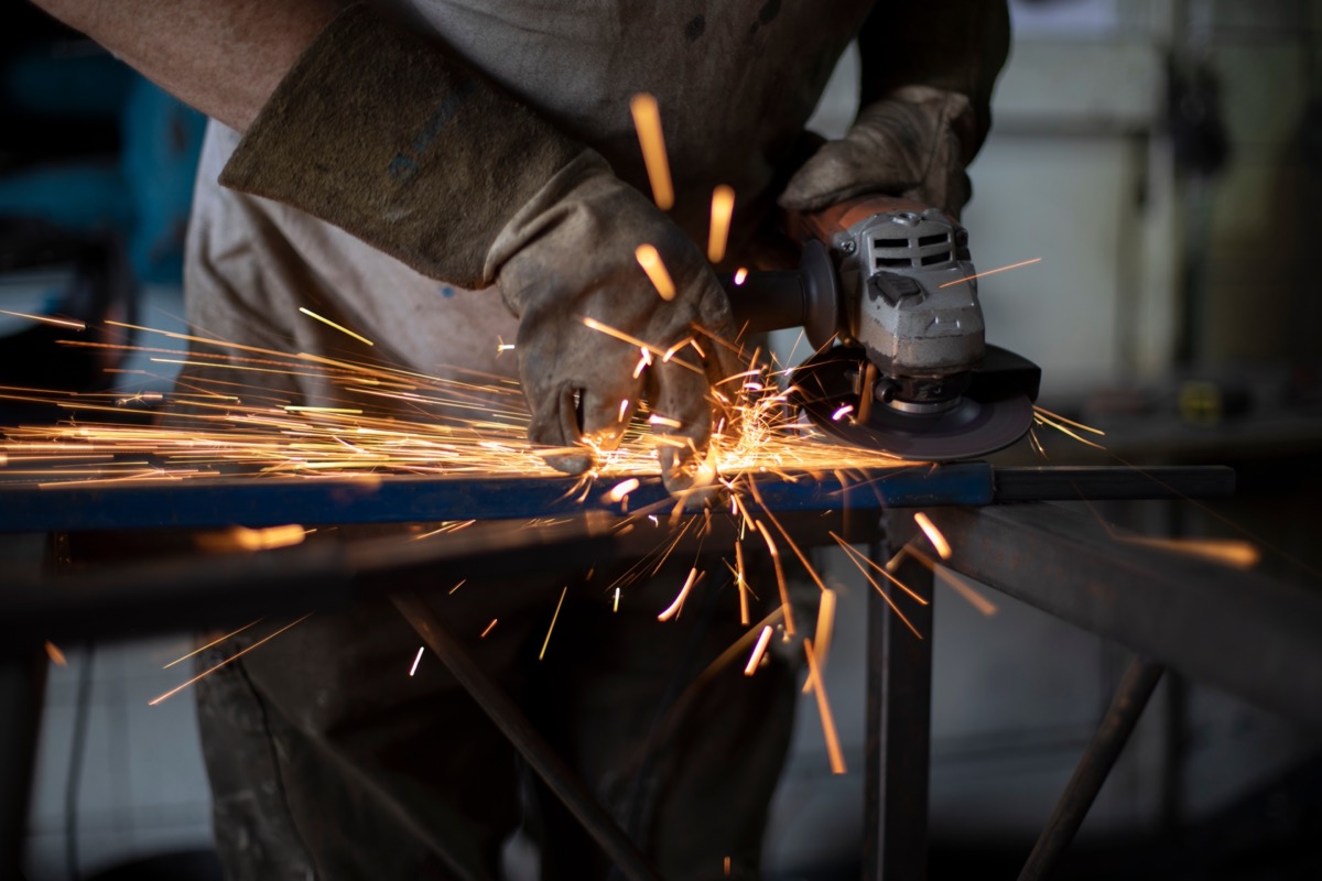 Work grinding machine. Sparks from the force of friction. A man in a workshop processes metal. Creation of a steel part.