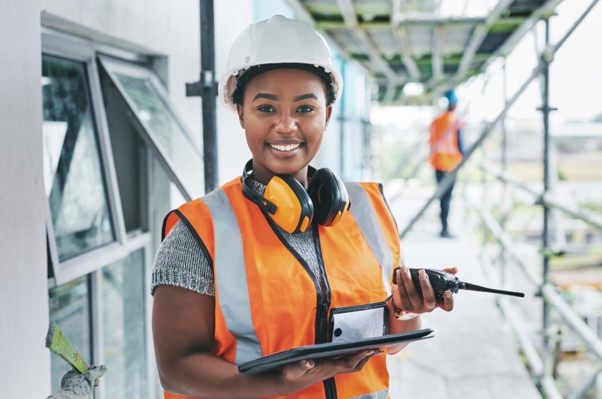 Smiling construction worker managing site logistics on tablet; financing concept