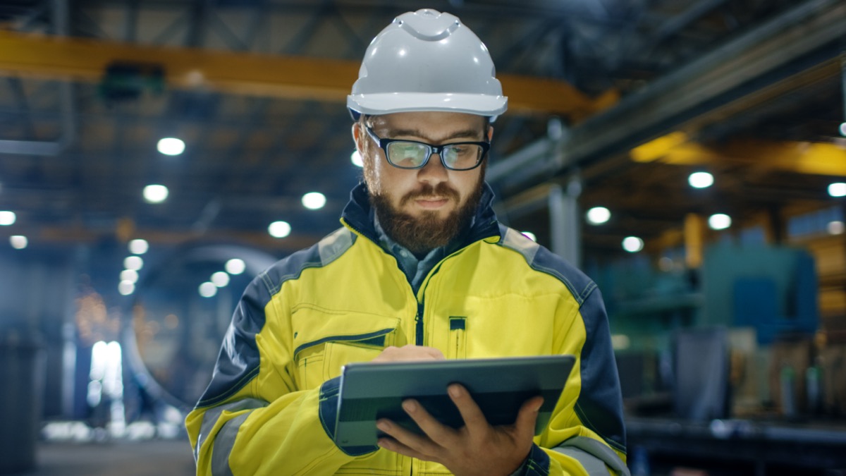 Industrial Engineer in Hard Hat Wearing Safety Jacket Uses Touchscreen Tablet Computer at Heavy Industry Manufacturing Factory; financing concept