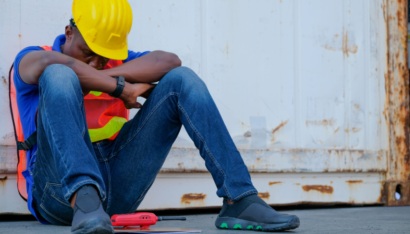 Construction worker sitting on the ground, head in arms; job-related stress concept