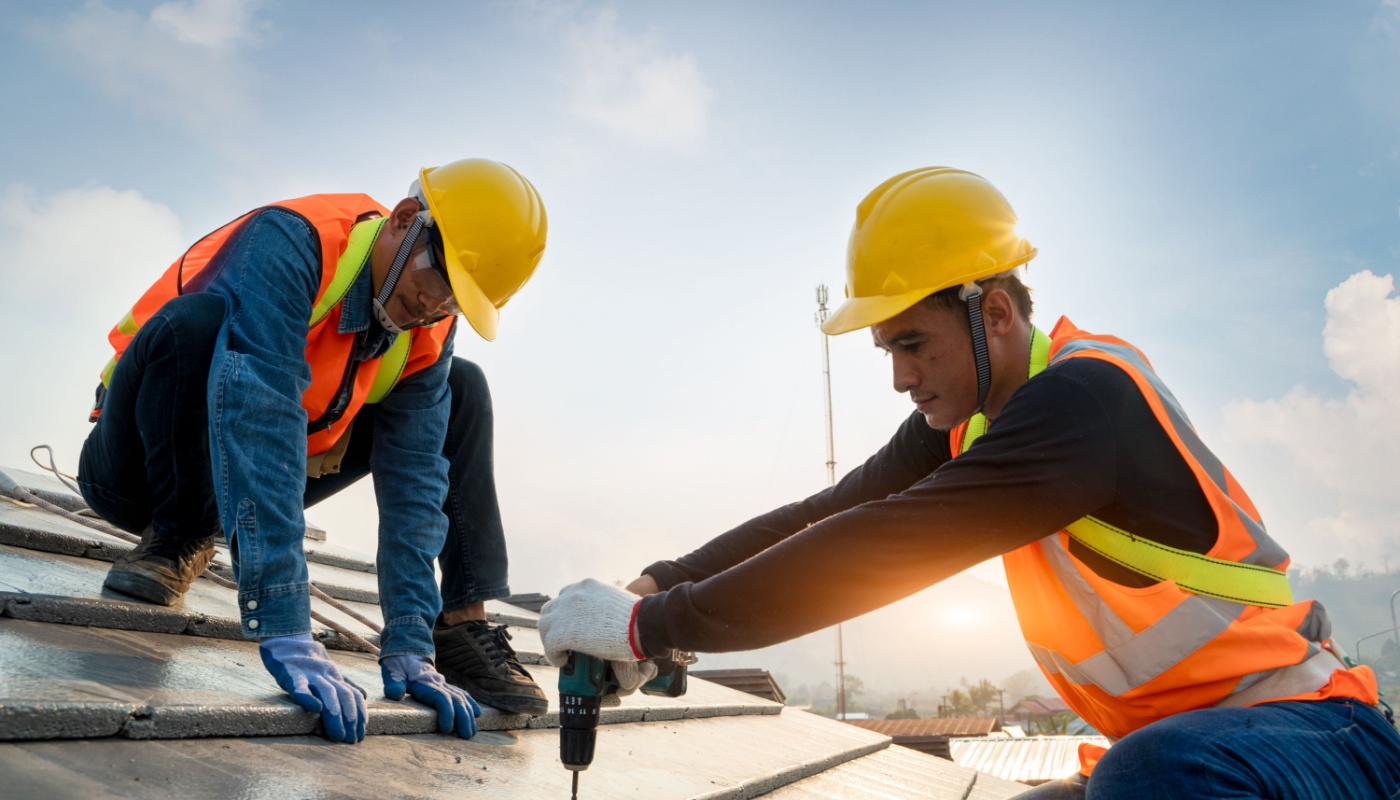 Construction workers wearing safety harness belts and hard hats on roof of building at a construction site; rework concept