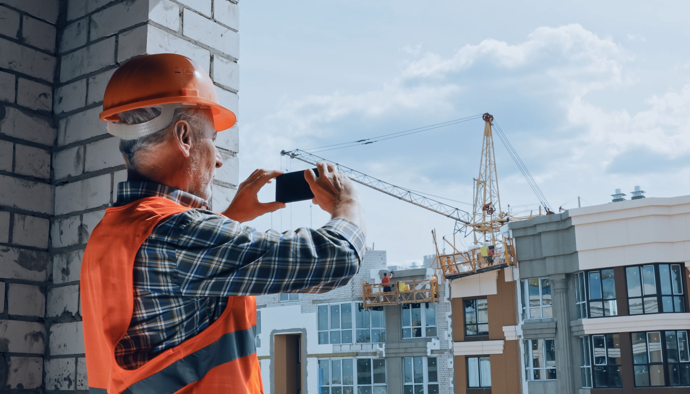 Builder taking photo with smartphone on construction site; trades contractors paid concept