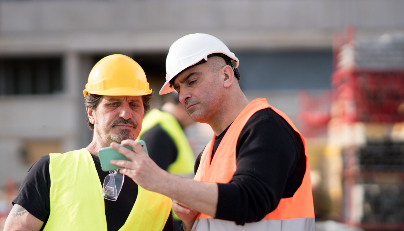 Construction workers at work on construction site using a phone for information; project risk concept