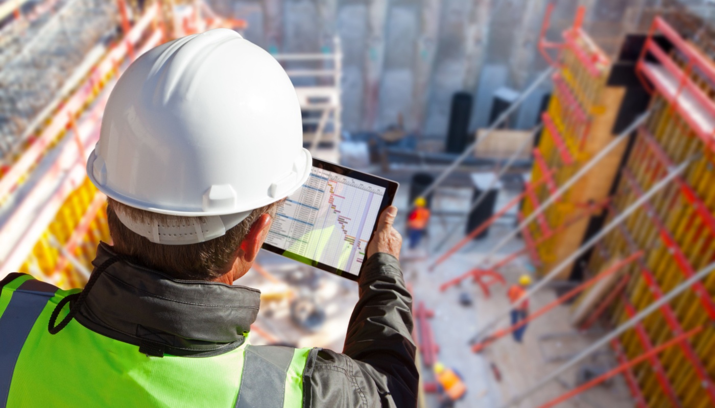 Civil engineer or architect with hardhat on construction site checking schedule on tablet computer; trade contractors concept