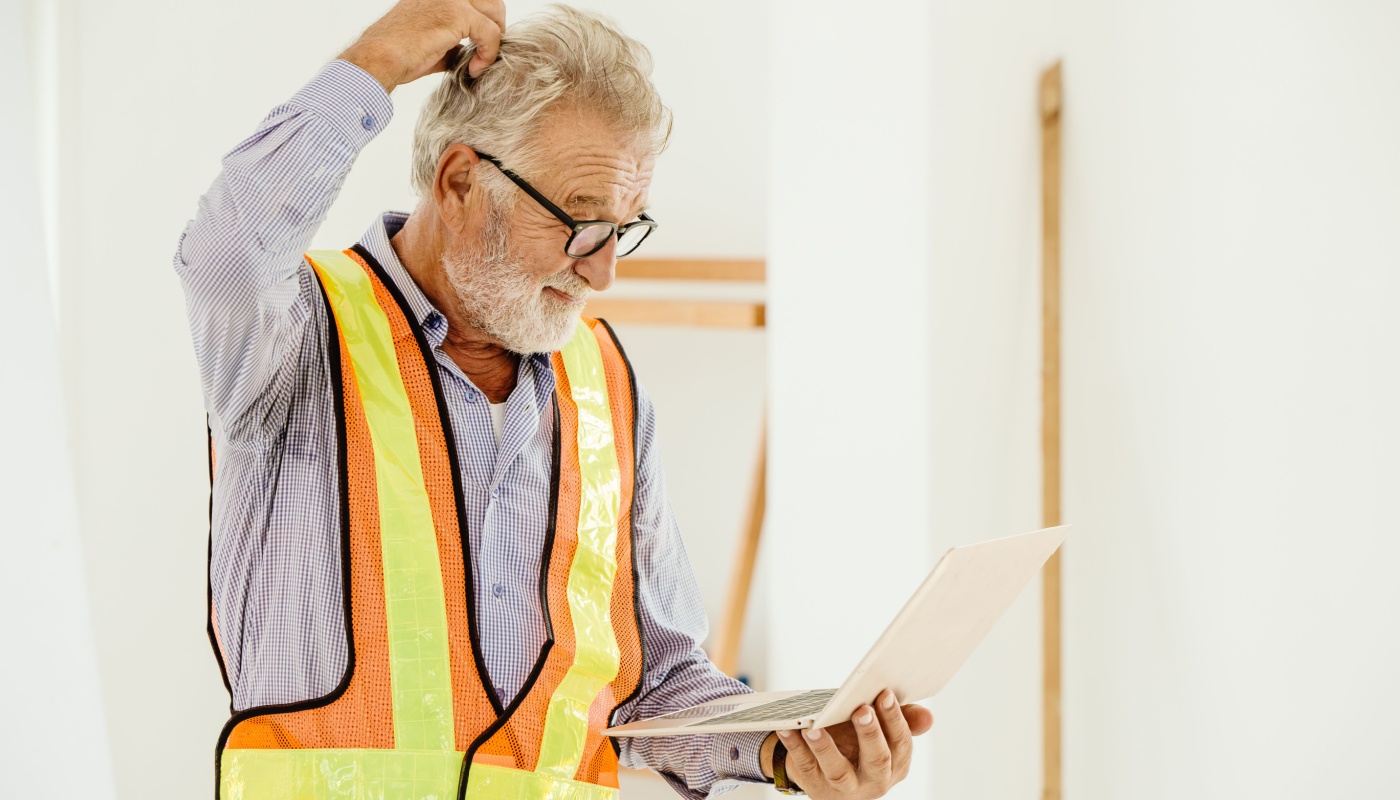 Worker on site scratching his head, looking at laptop; feature hype concept