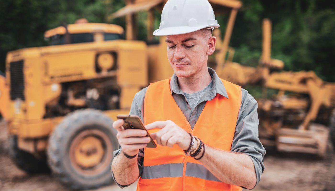 Construction worker in hardhat using smartphone on site; feature hype concept