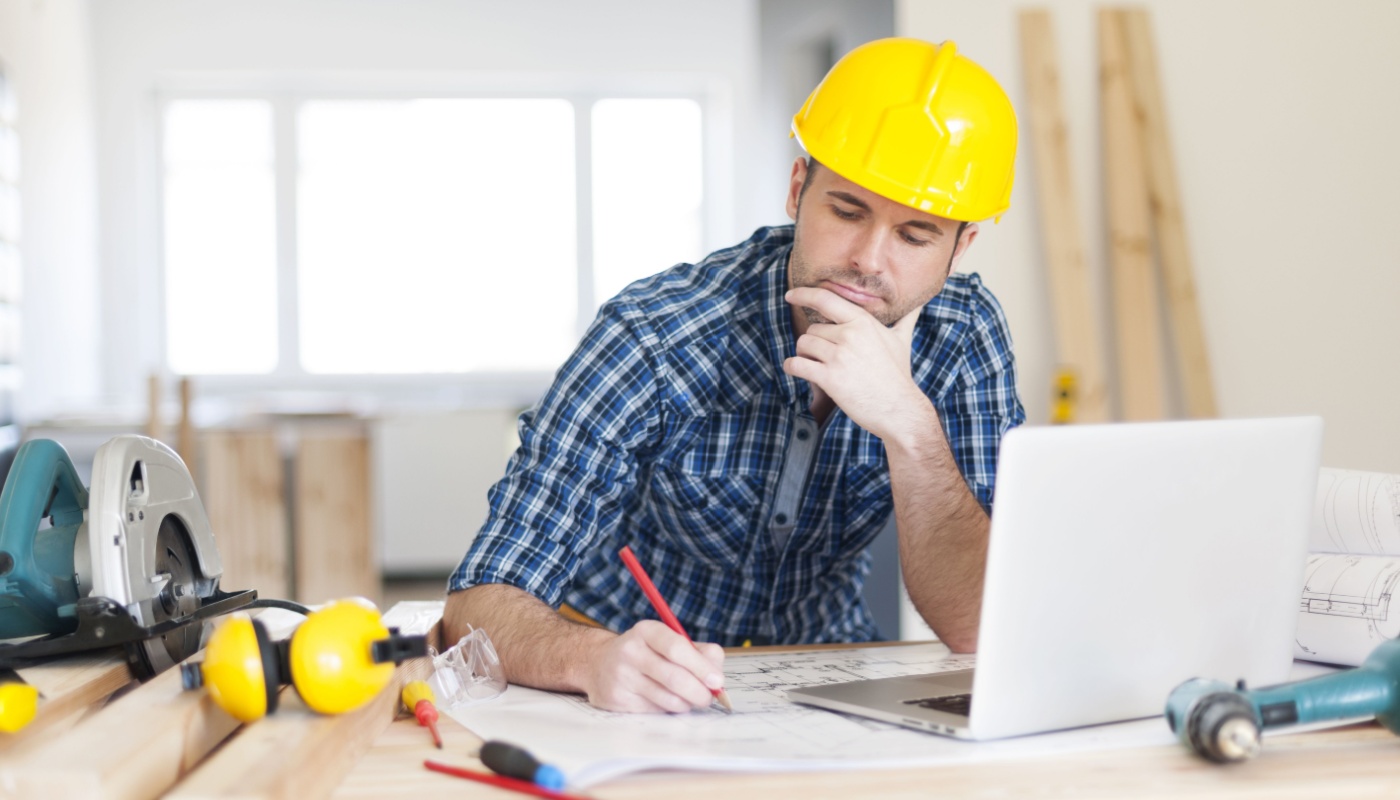 Construction worker in hard hat, working on a plan at a table, with laptop; feature hype concept