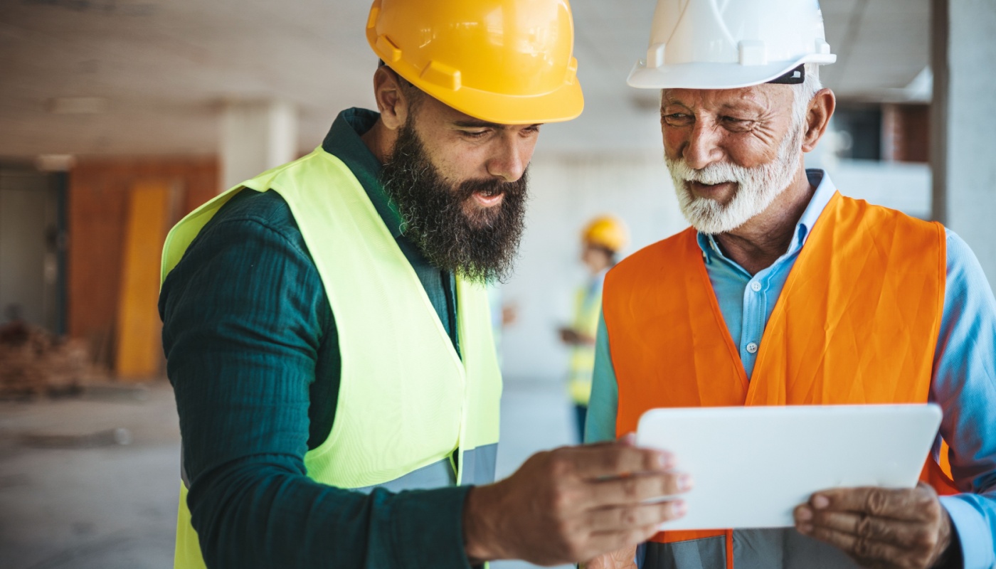 Trade workers in hard hats using tablet on site; tech resistance concept