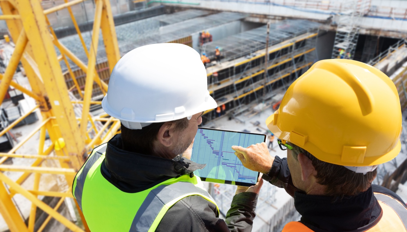 Workers on construction site using tablet; construction management software concept