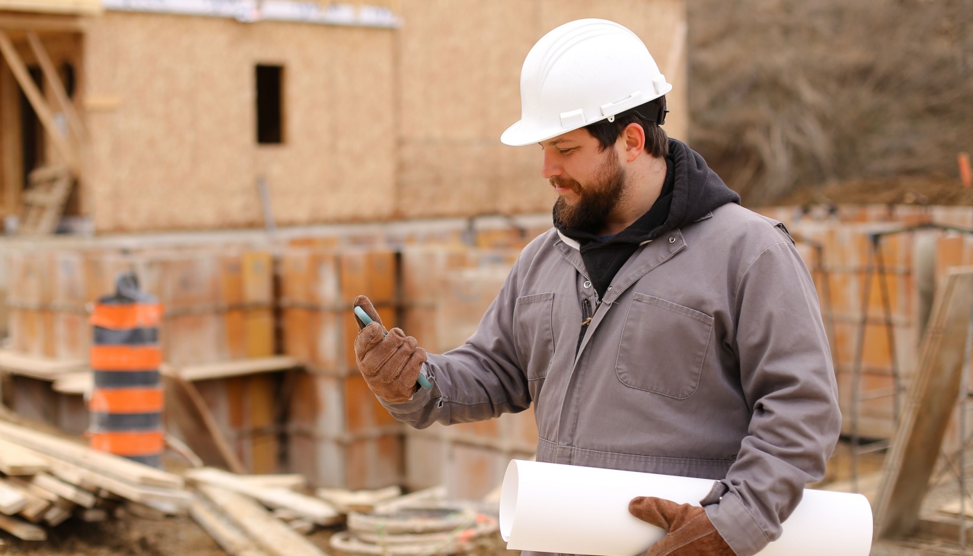 Worker in hardhat on construction site, using smartphone; construction management software concept