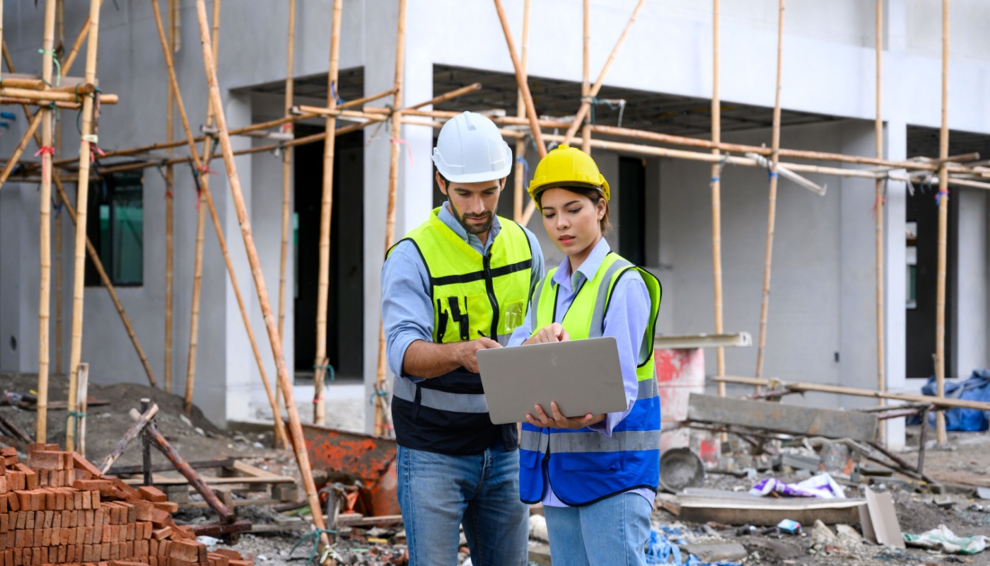 Construction workers in vests and helmets working with laptop, at a building site; construction leadership concept